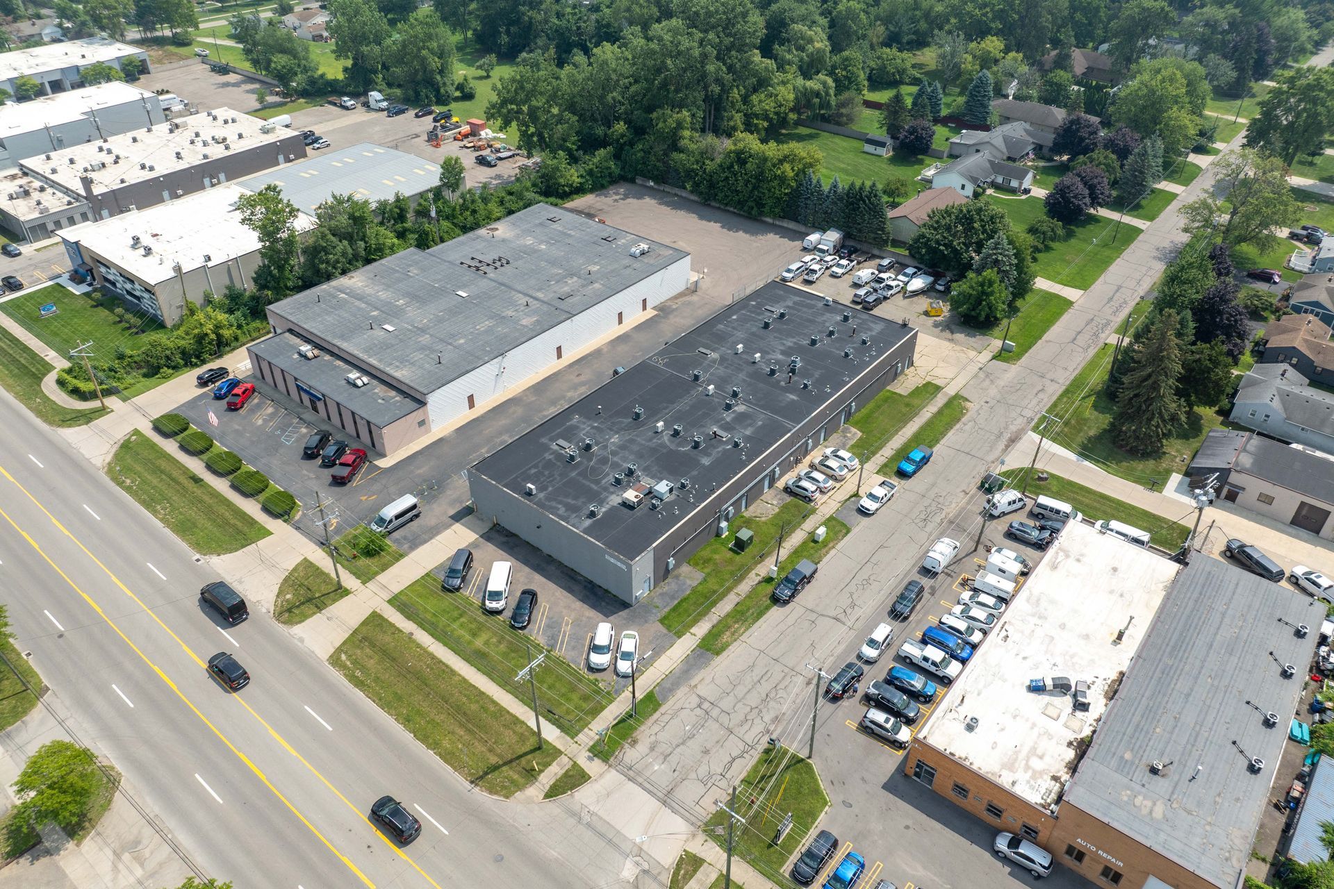 Aerial view of two industrial buildings with parking and a street, next to residential homes.
