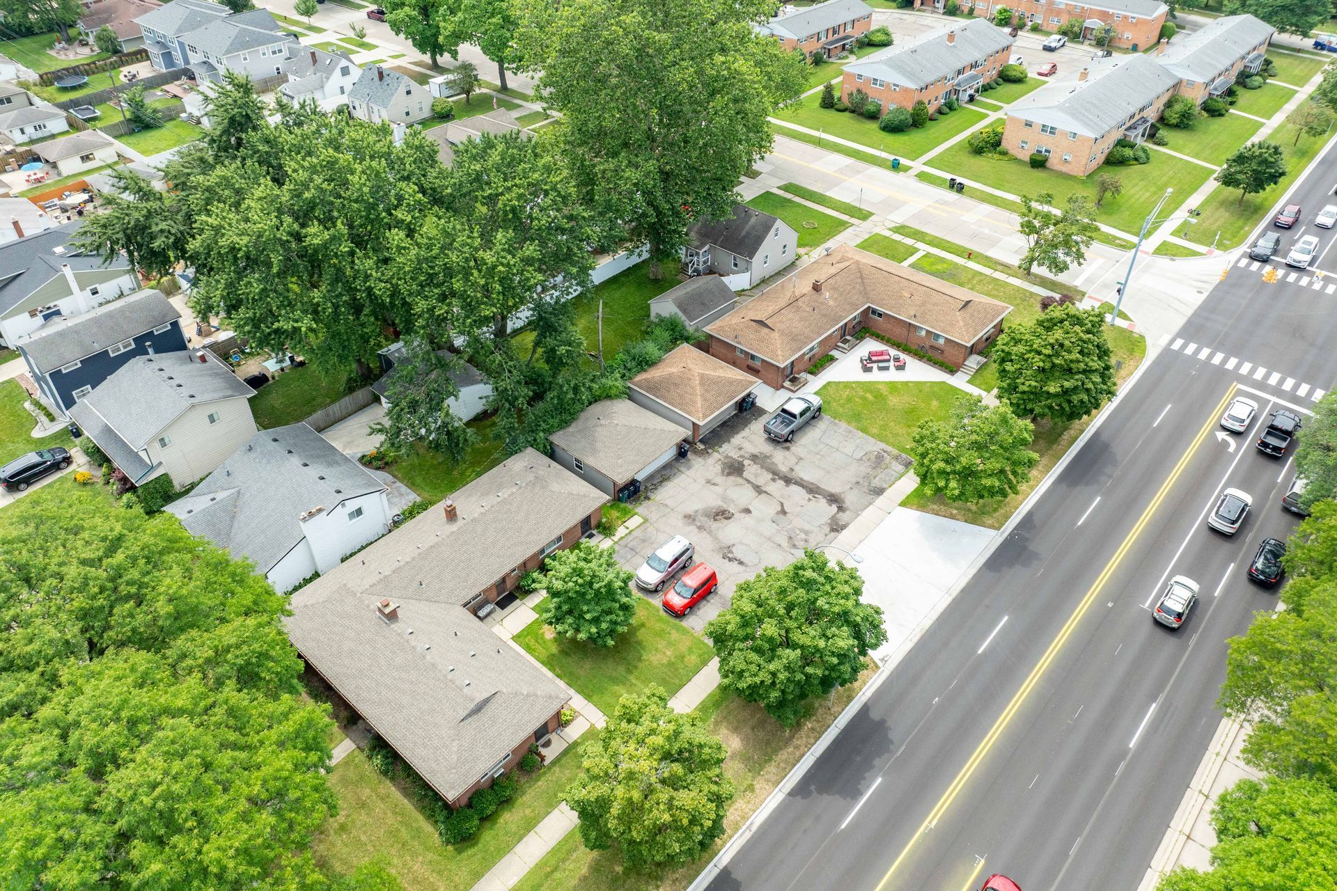 Aerial view of a street with houses, trees, and cars on the road.