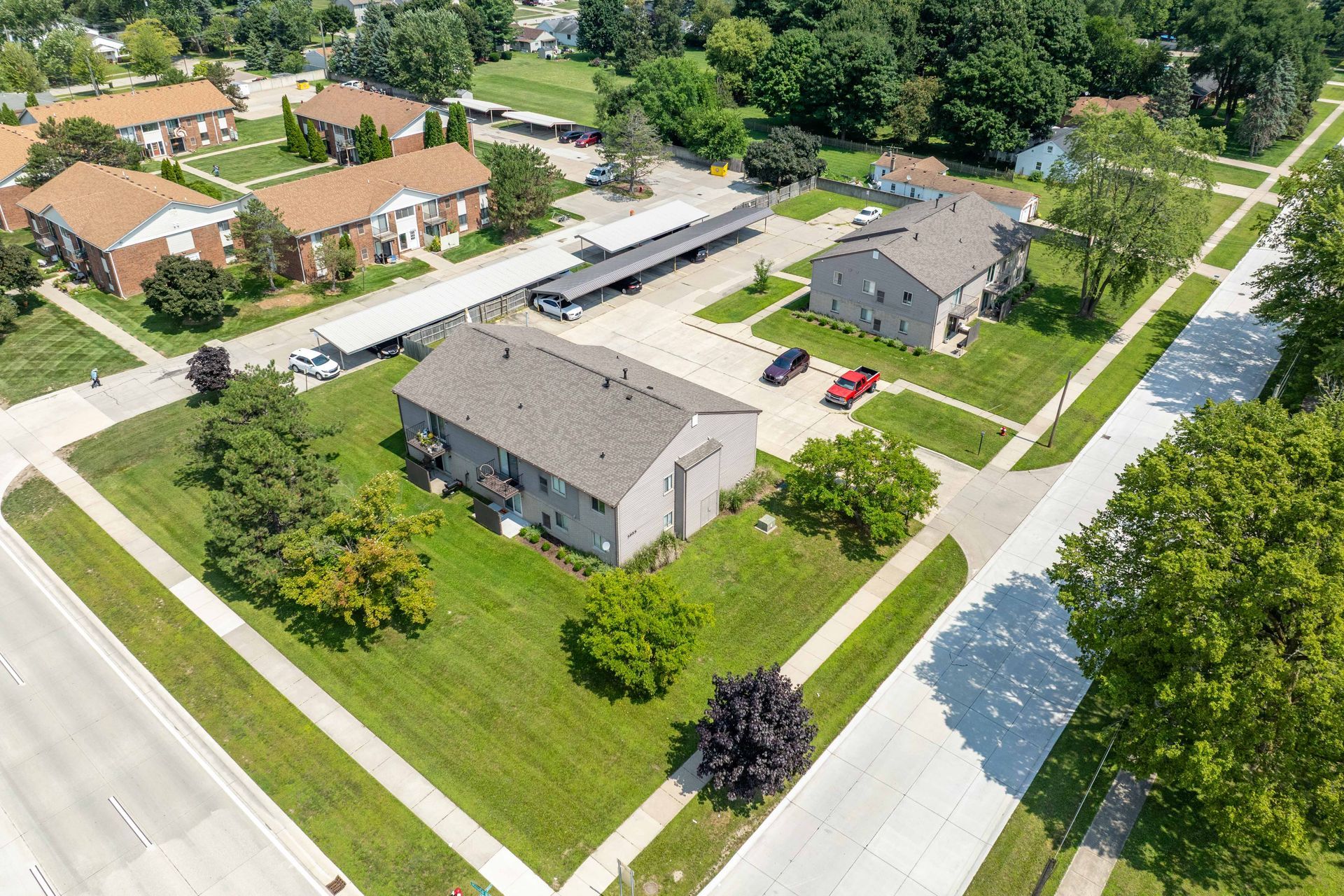 Aerial view of a residential area with buildings, green lawns, roads, and trees on a sunny day.