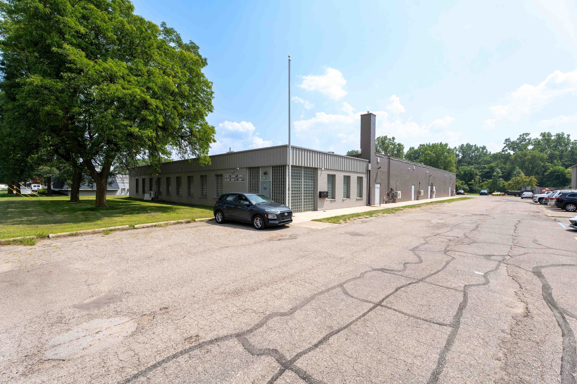 Gray concrete building with a chimney, car parked out front, and cracked asphalt in a grassy area.