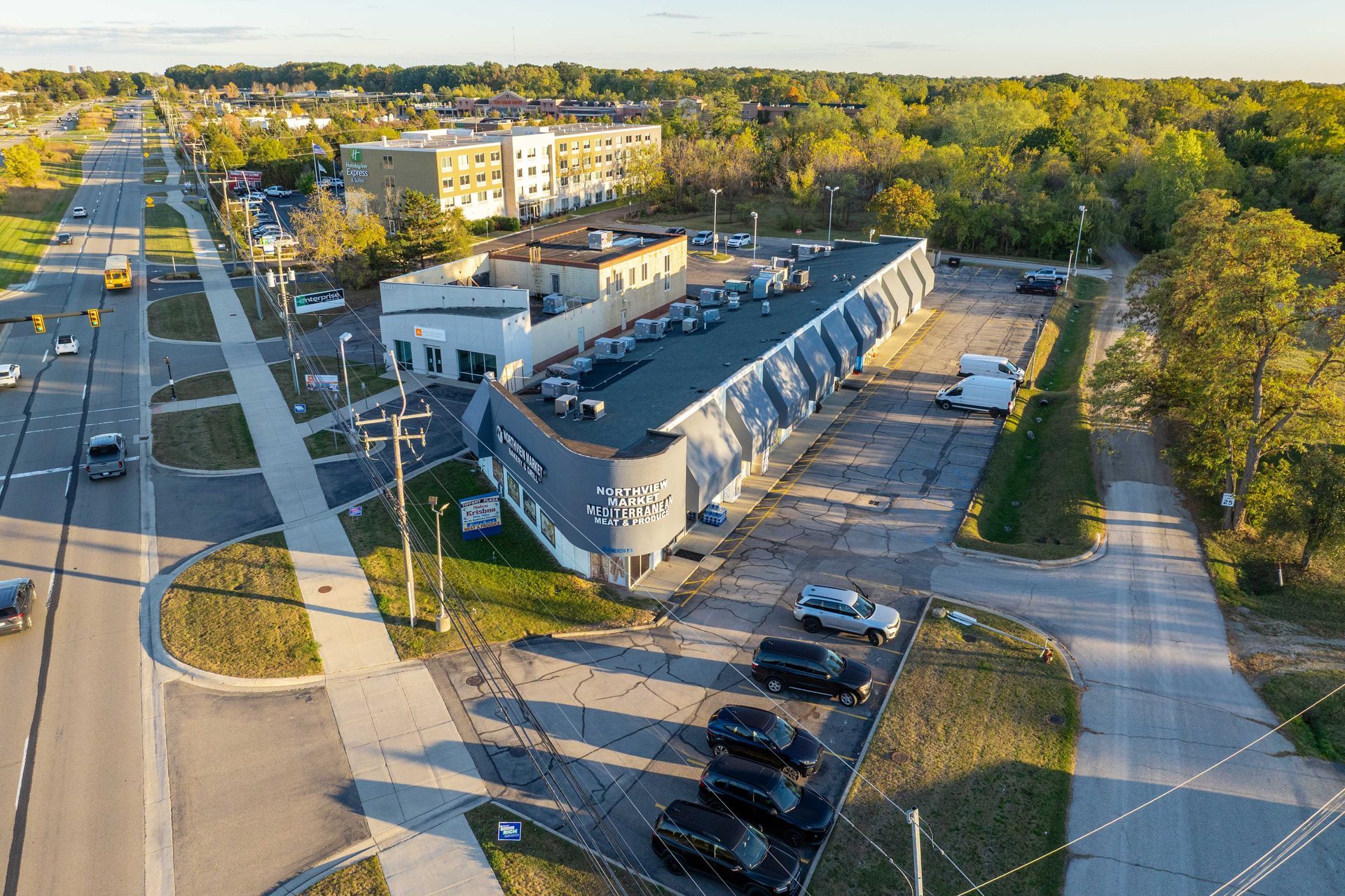 Aerial view of a commercial building with a long, curved design; beside a multilane road and parking lot.
