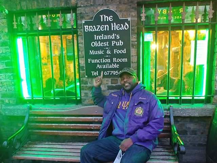 A man sitting on a bench in front of a sign that says the brazen head
