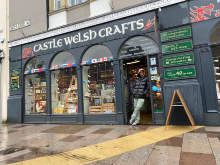 A man is standing in front of a store called castle welsh crafts.