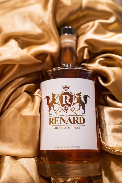 A bottle of renard whiskey is sitting on a gold cloth.