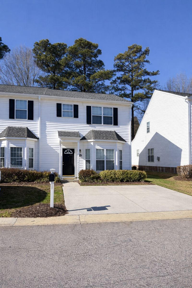 A two-story, white-sided townhouse with black shutters and bay windows, under a clear blue sky.