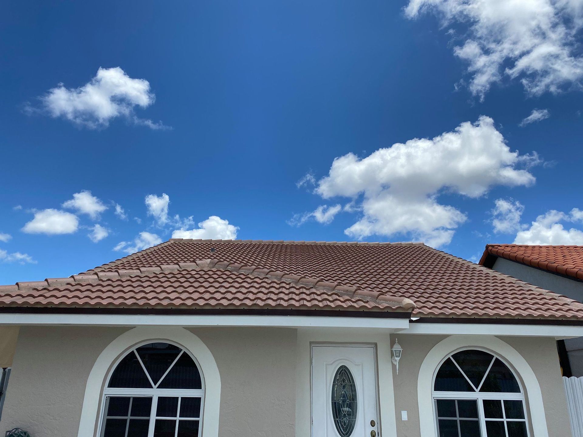 Single-story house with red tile roof and white walls under a bright blue sky with clouds