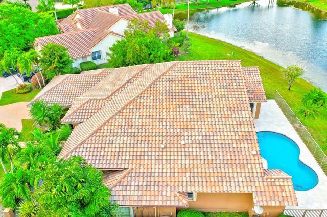 Aerial view of a house with a tiled roof beside a blue backyard pool and lakefront greenery