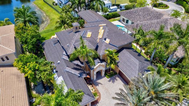 Aerial view of a large tropical house with dark tile roof, surrounded by palm trees and lush greenery.