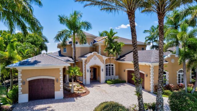 Large Mediterranean-style house with palm trees, stone driveway, and arched entryway under a bright blue sky