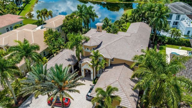 Aerial view of a tropical luxury home with tiled roofs, palm trees, and a driveway near water.