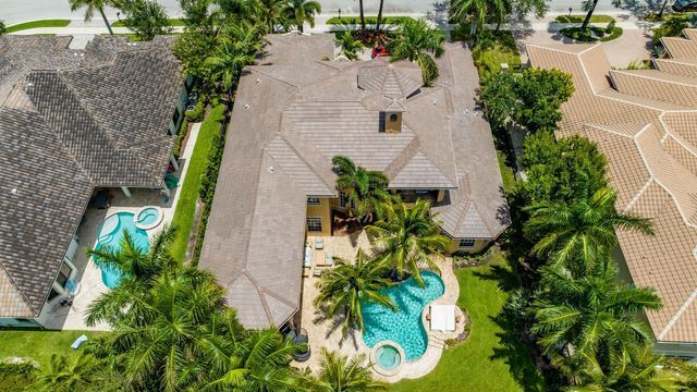 Aerial view of a suburban house with a turquoise backyard pool, palm trees, and neighboring homes