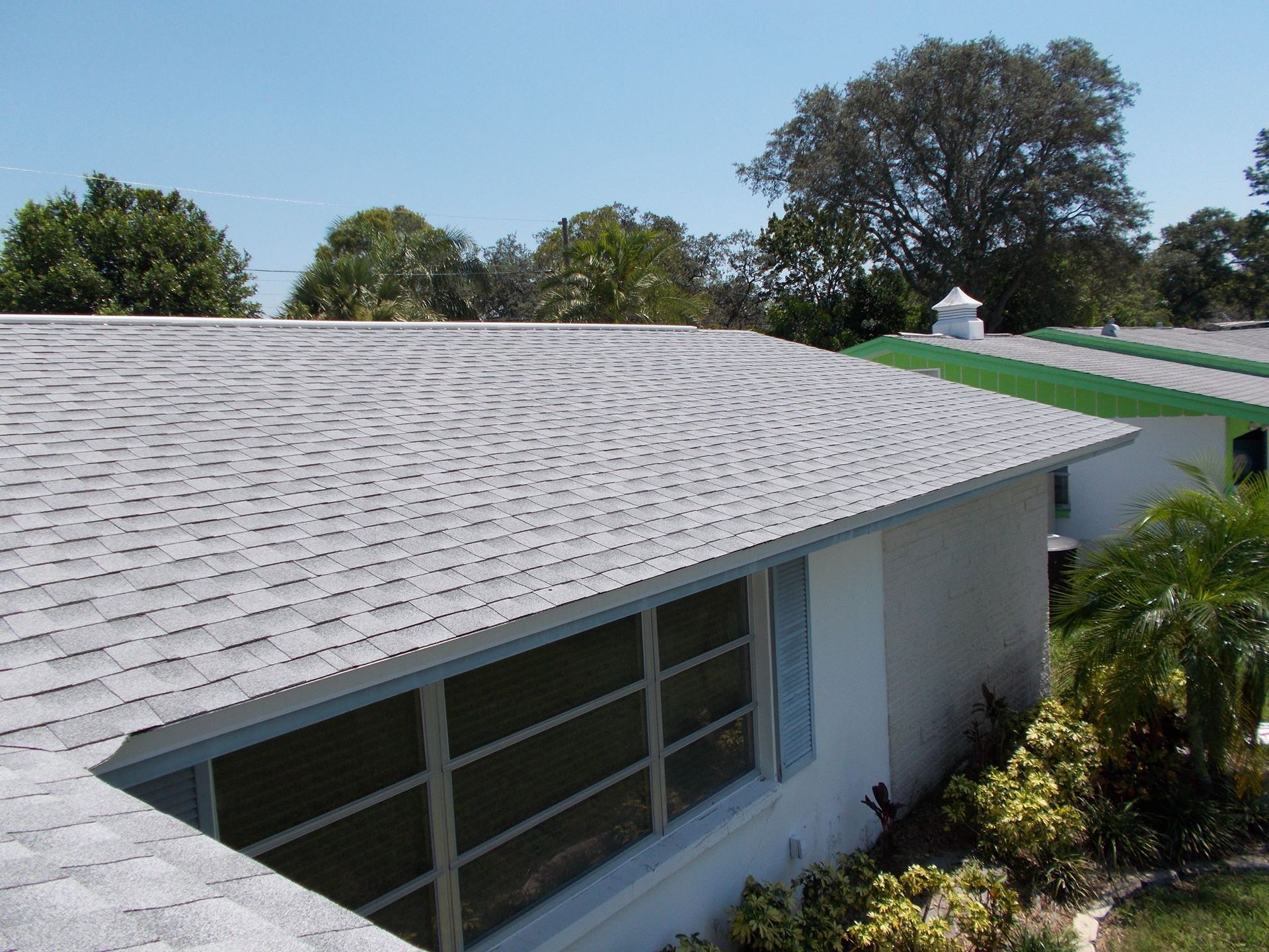 White house roof with skylight and green awning, viewed from above amid trees and clear sky