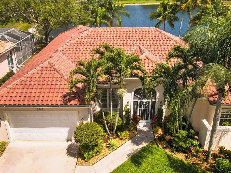 Aerial view of a tropical house with a red tile roof, palm trees, and a driveway by the water