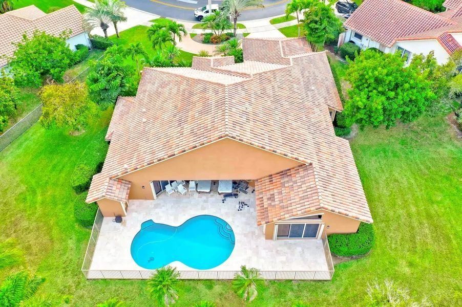 Aerial view of a tan-roofed house with a backyard pool and green lawn.