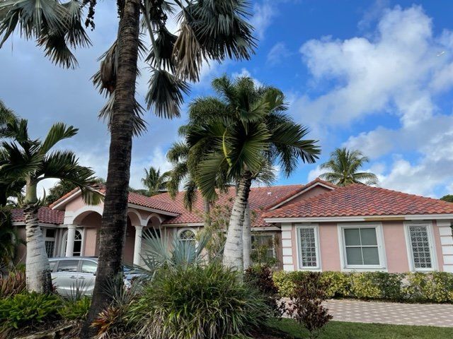 Single-story pink house with red tile roof, palm trees, and a white car in the driveway