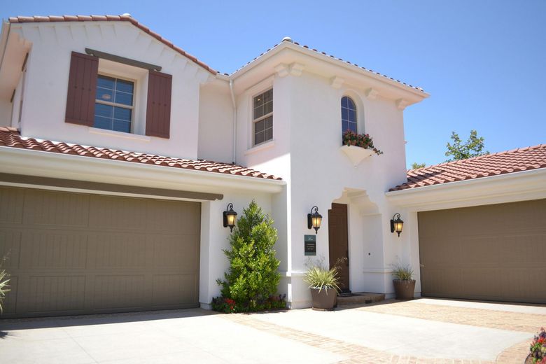 White stucco house with terracotta roof tiles, two attached garages, and a sunny driveway.