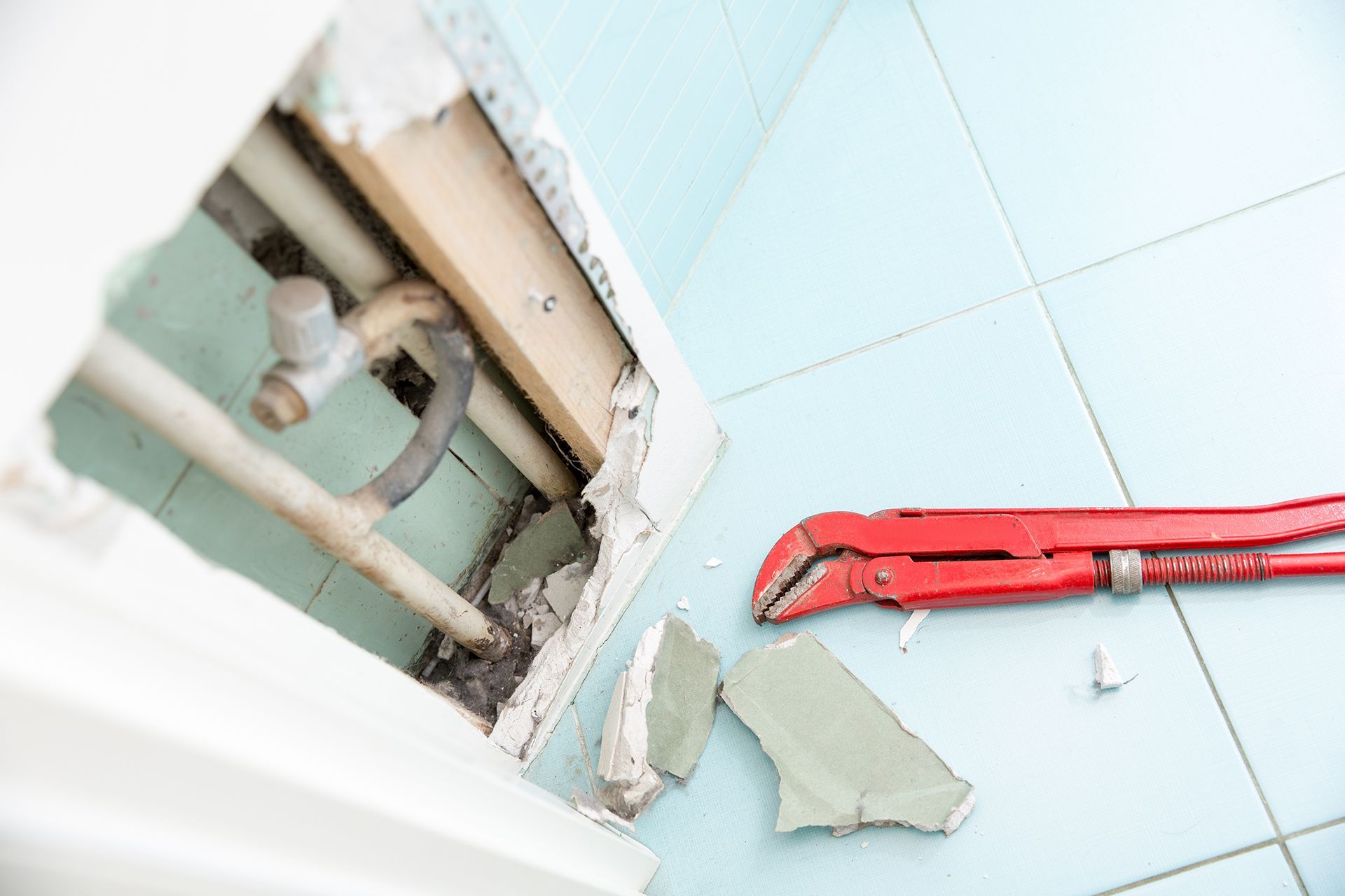 A wrench is laying on the floor next to a hole in the wall