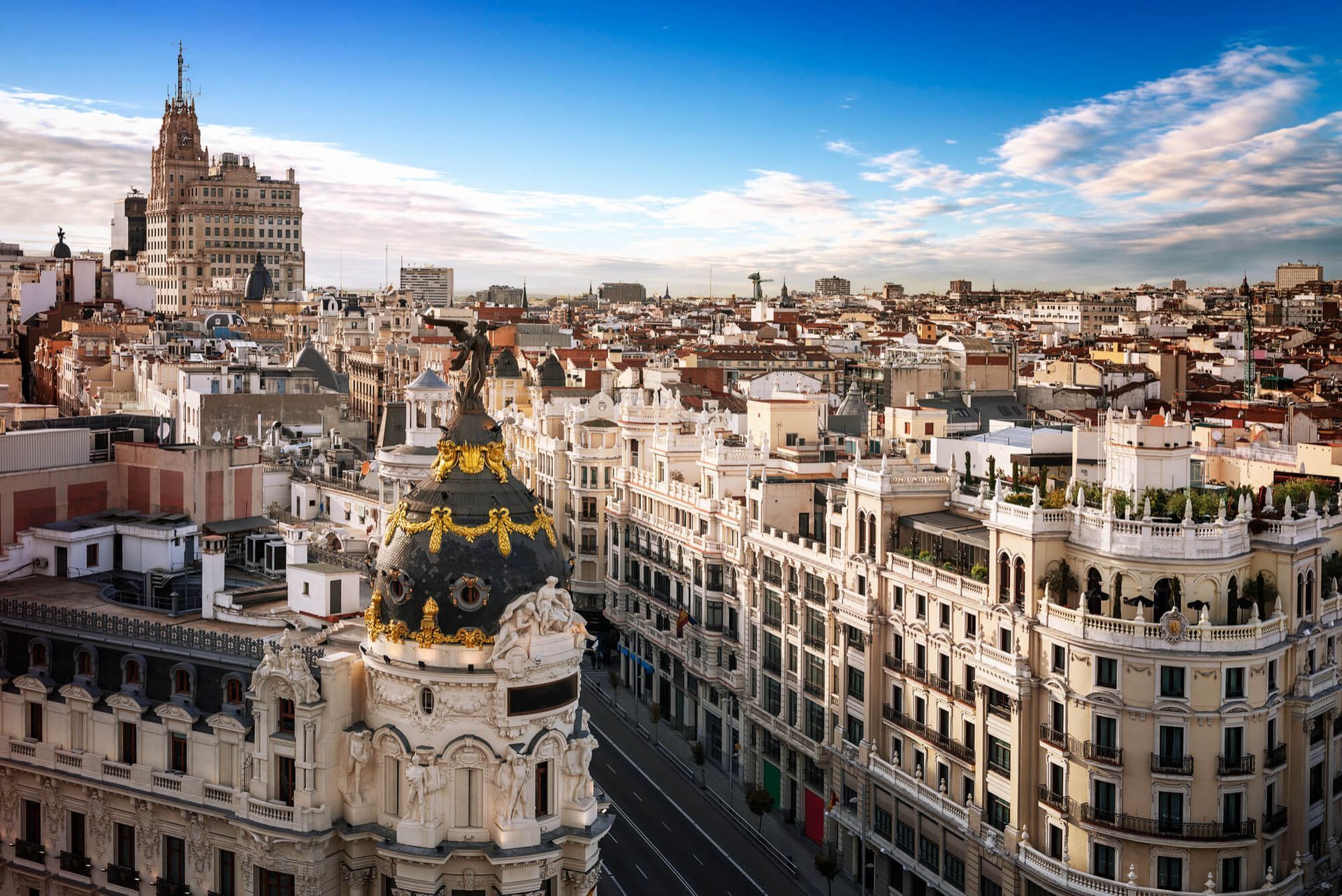 Paisaje urbano de Madrid con edificios históricos y la cúpula de la Metrópolis bajo un cielo azul.
