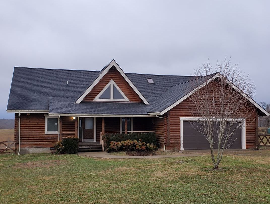 A log cabin with a gray roof is sitting in the middle of a grassy field.