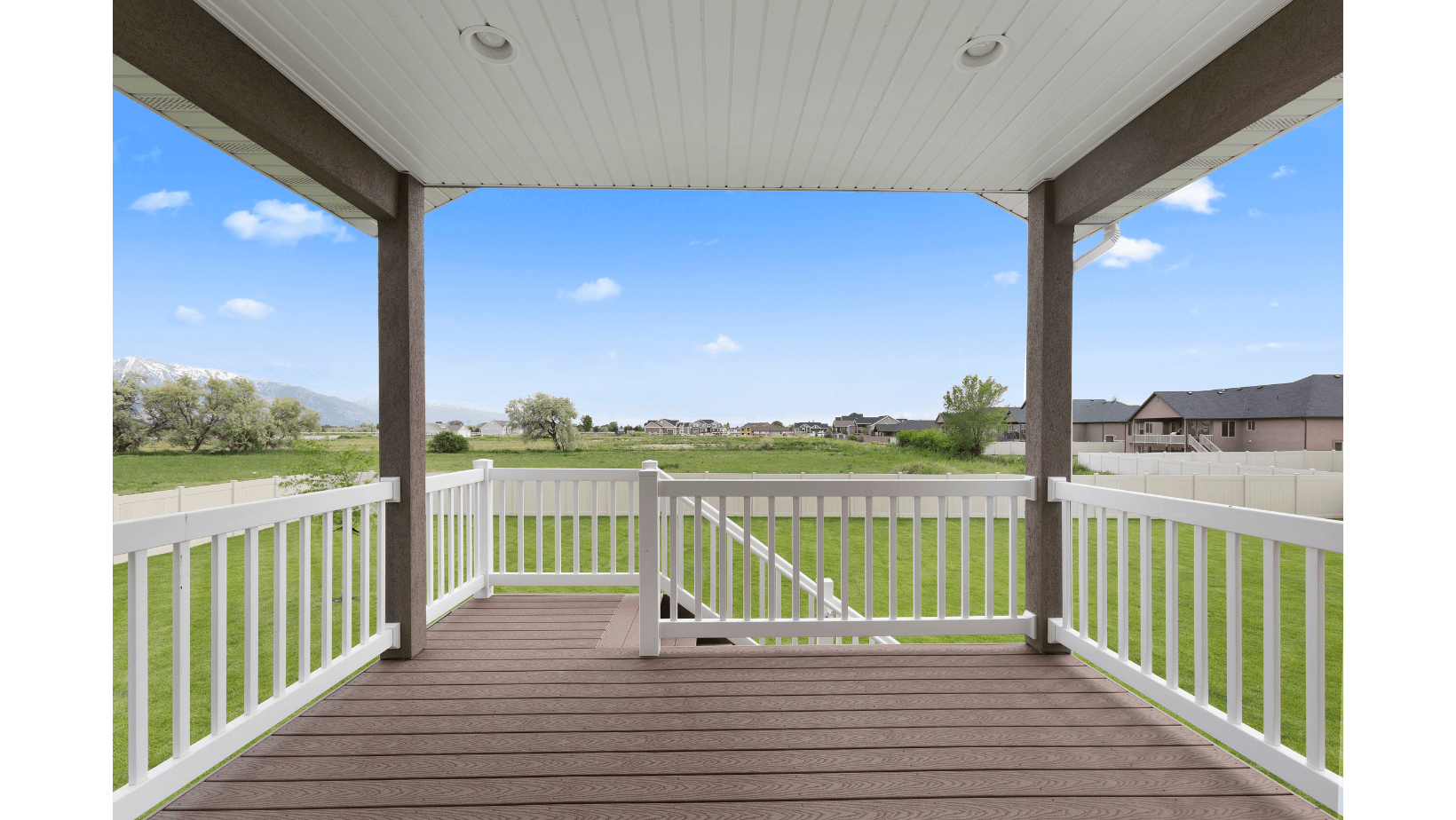 An empty porch with a white railing and a view of a field.