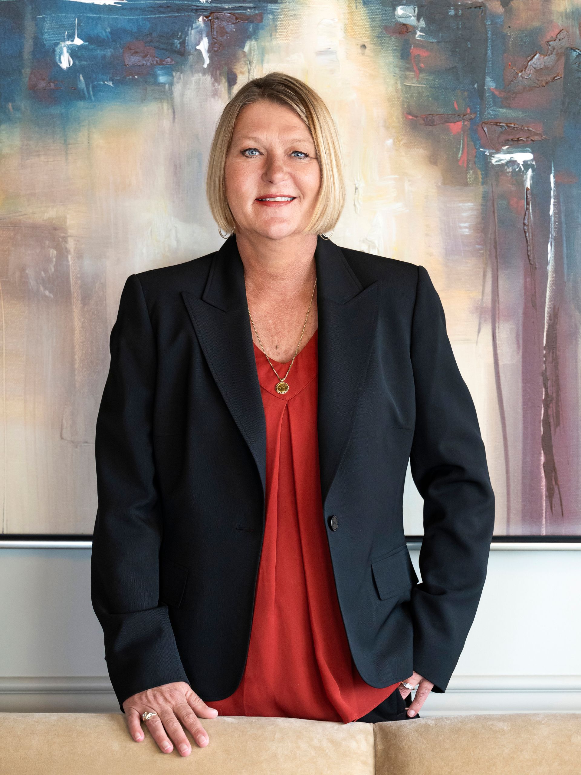 Kristy Lindsay with blonde hair is wearing a black jacket and smiling.