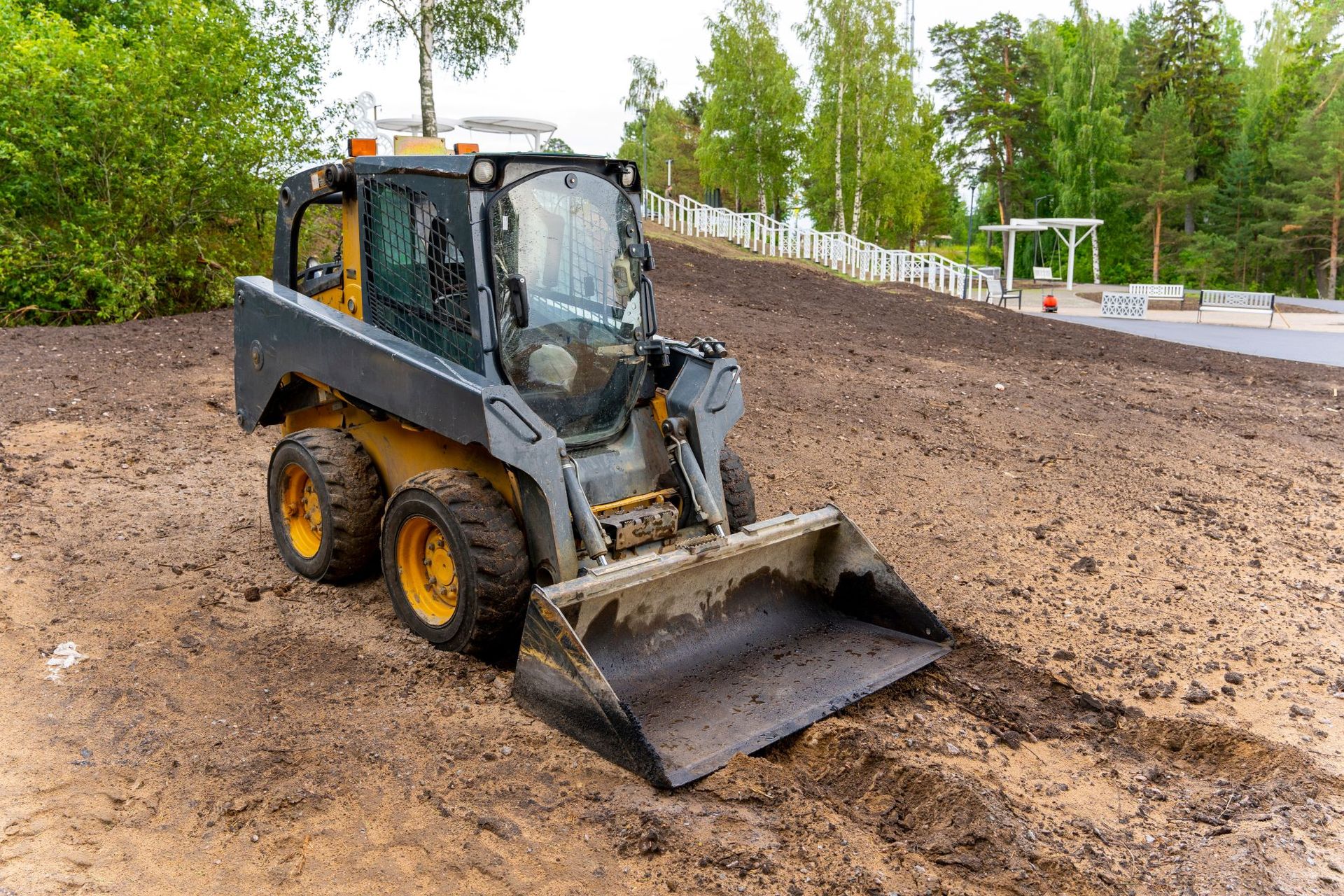 Compact loader with bucket leveling dirt on a muddy construction site