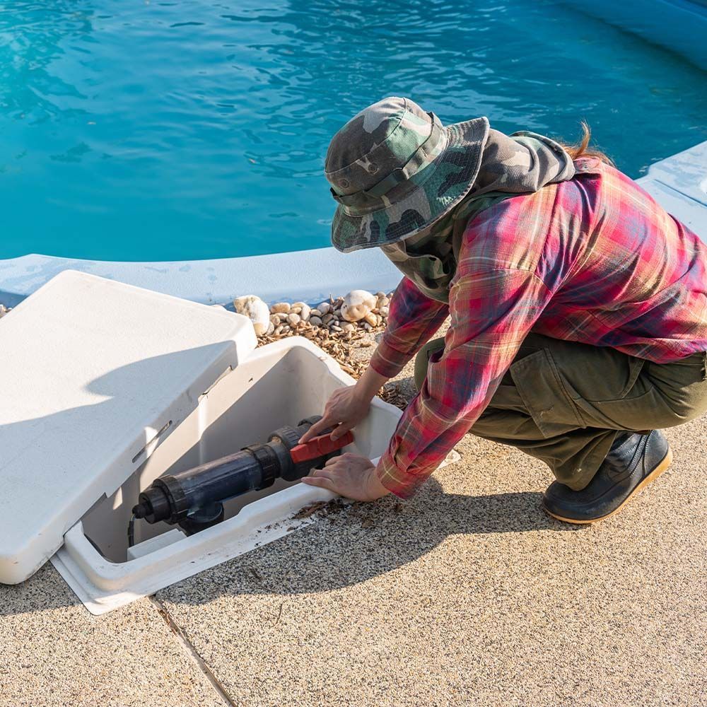 Worker in plaid shirt using power tool to repair a dock beside blue water