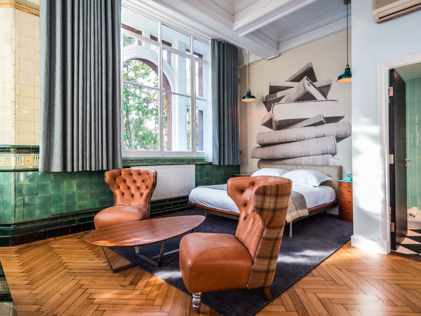 Hotel room with bed, two brown leather chairs, coffee table, large window, and mural.