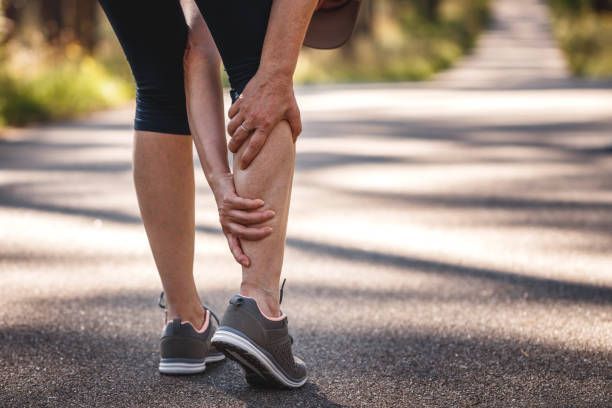 A woman is holding her leg in pain while walking down a road.