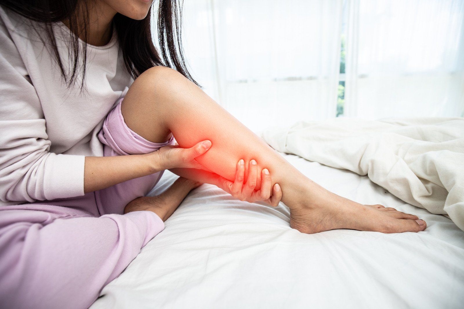 A woman is sitting on a bed holding her leg in pain.