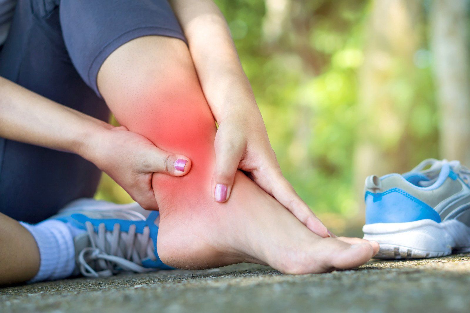 A woman is sitting on the ground holding her ankle in pain.