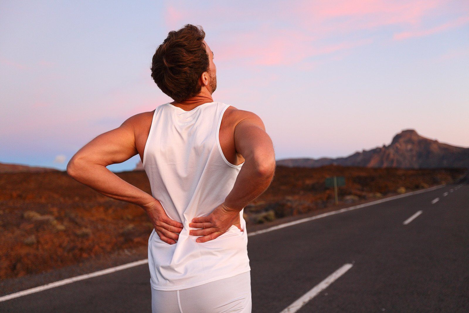A man is standing on the side of a road with his hands on his back.
