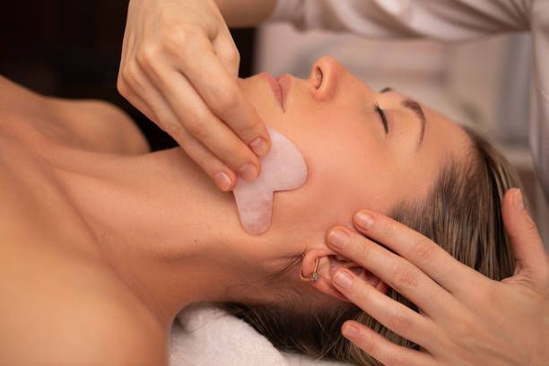 A gua sha tool is used on a person's cheek during a facial treatment.
