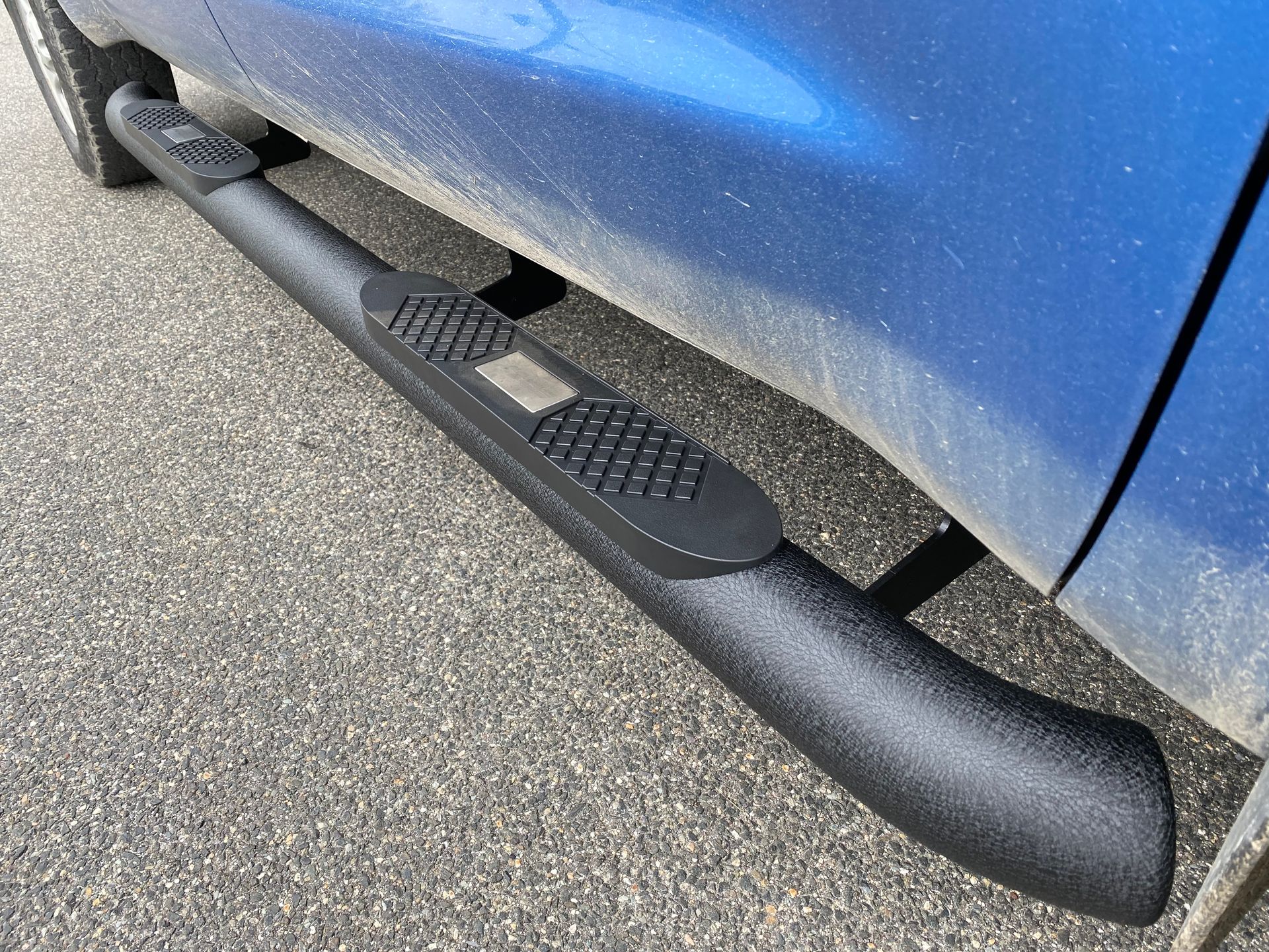 A blue truck with black side steps is parked on the side of the road.