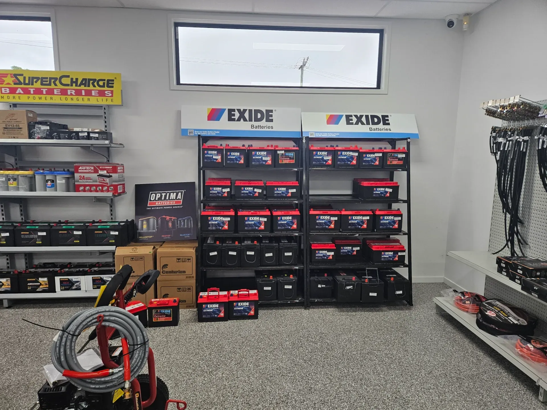 Interior of a retail store with shelves stocked with automotive batteries, including Exide and SuperCharge brands.