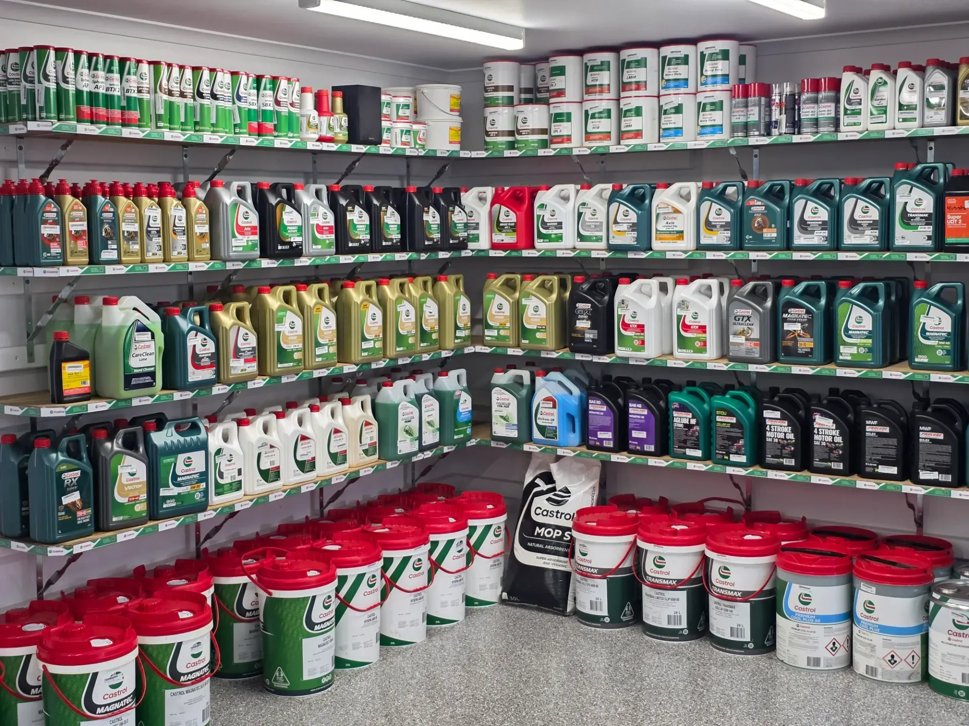Shelves stocked with various motor oil containers and large white buckets in a brightly lit retail store.
