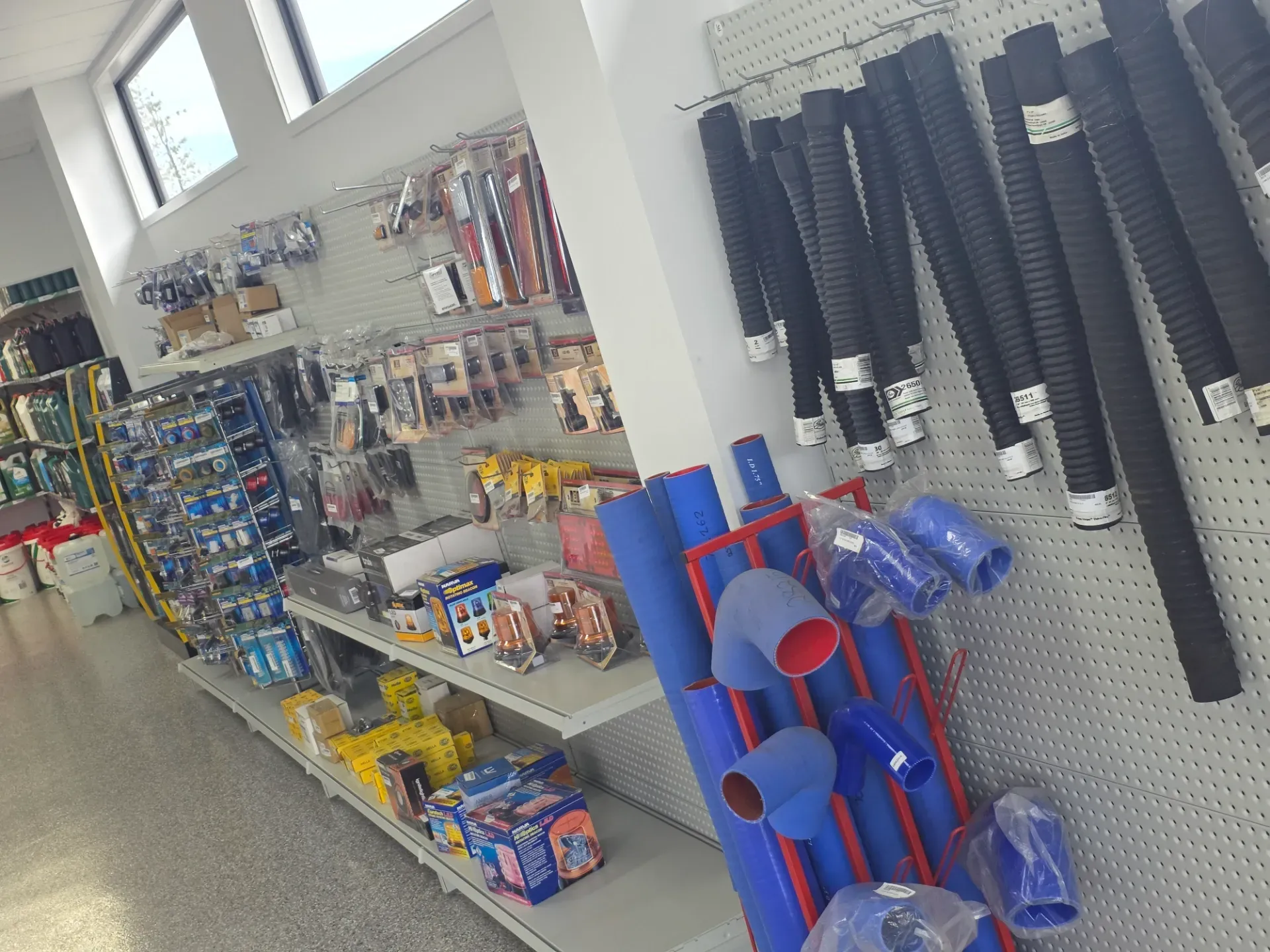A retail store aisle featuring various automotive hoses and piping components displayed on shelves and pegboards.