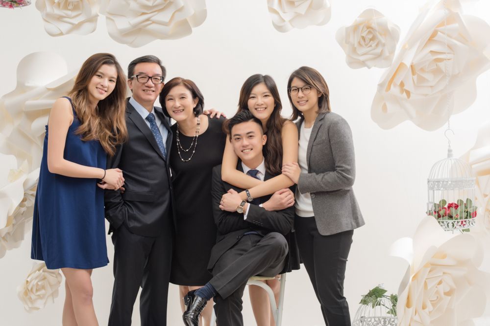 A family is posing for a picture in front of a wall of paper flowers.