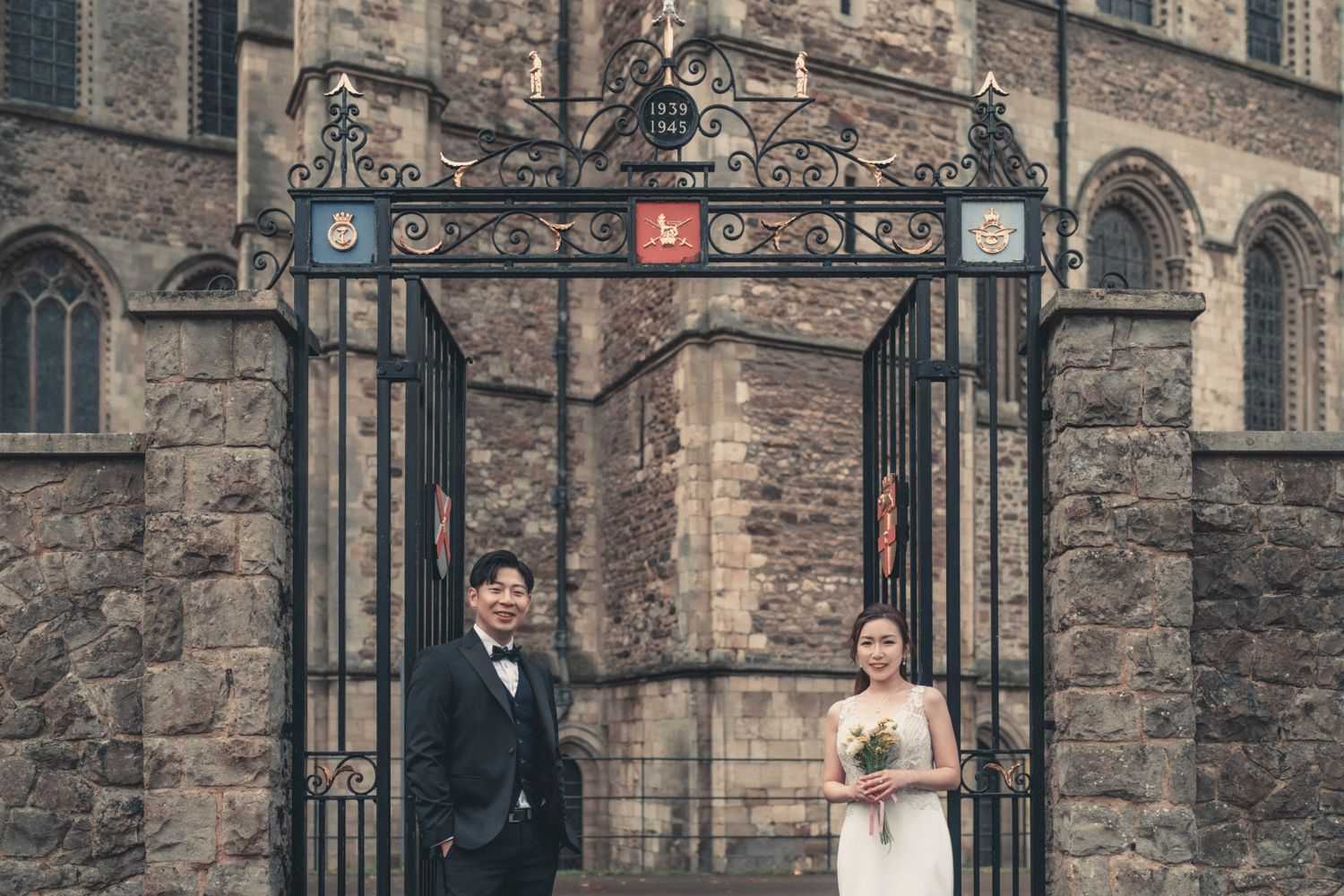 A bride and groom are posing for a picture in front of a castle gate.