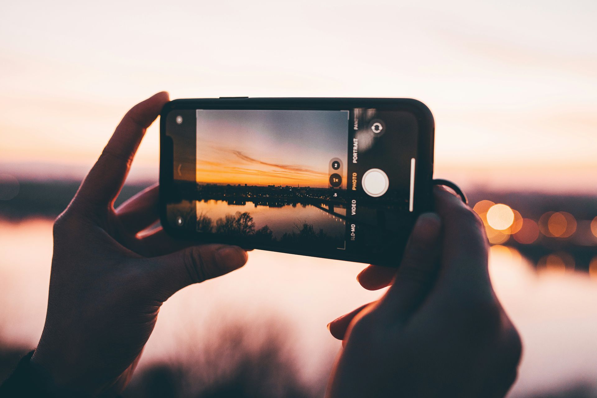 A person is taking a picture of a sunset with a cell phone.