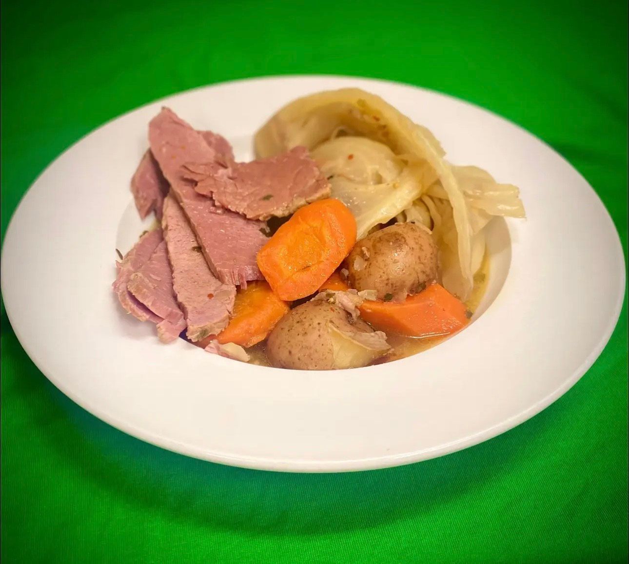 A white plate topped with corned beef , carrots , potatoes and cabbage.