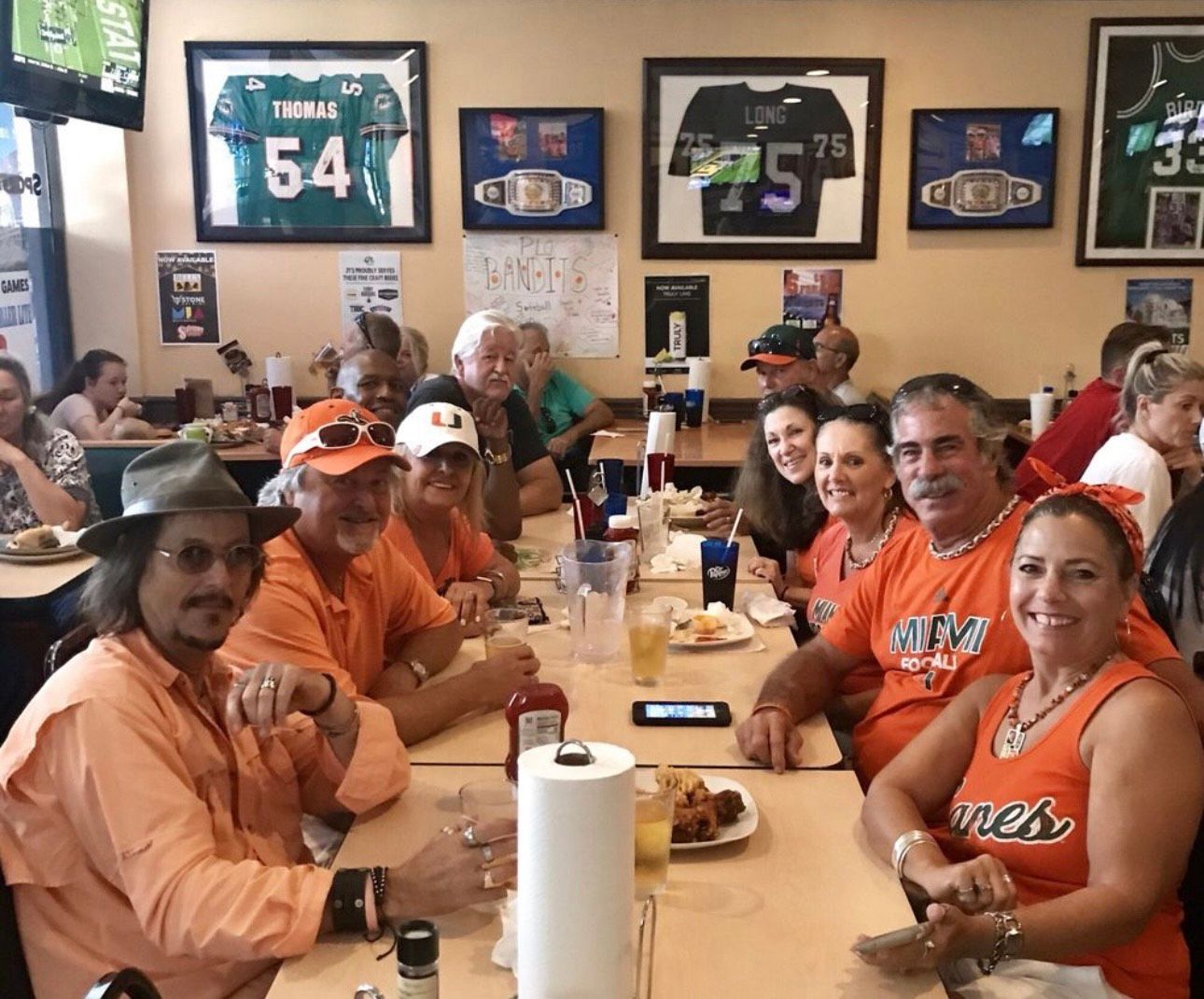 A group of people are sitting at tables in a restaurant wearing orange shirts with the number 54 on them