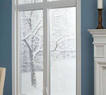 A window with a white frame looks out onto a snow-covered yard with trees, set against a blue wall near a white fireplace.