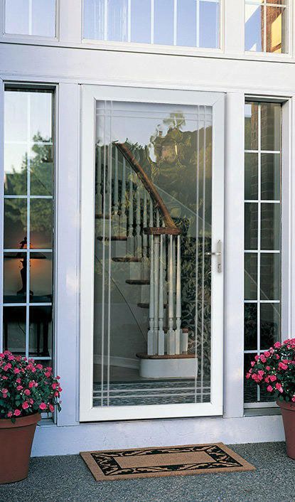 A white storm door with a full-length glass panel, flanked by two sidelights and potted pink flowers on a porch.