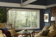 A cozy living room with a large window overlooking trees, featuring dark blue walls, light sofas, and a wooden coffee table.