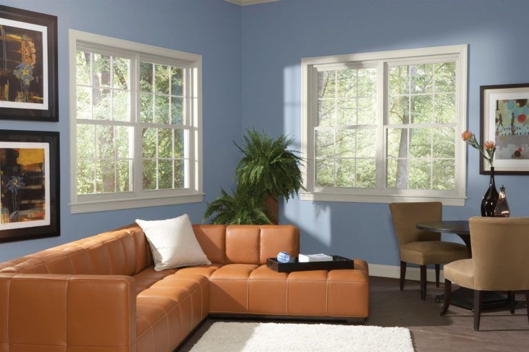 A living room with blue walls, a leather corner sofa, large windows, a dining table with chairs, and wall art.
