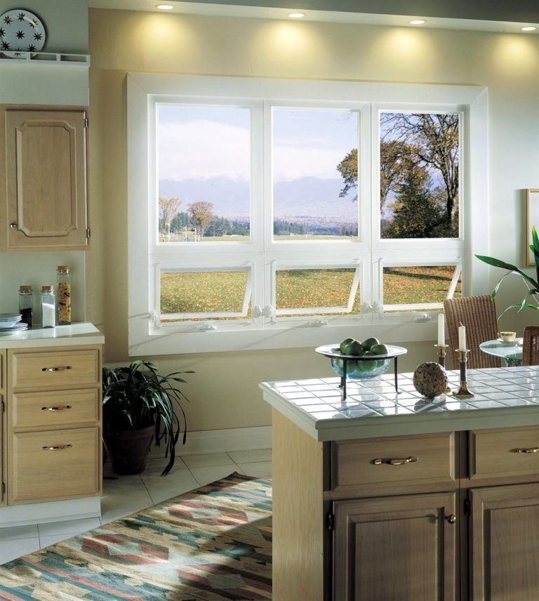 A bright, clean kitchen featuring light-wood cabinets, a tiled island, a houseplant, and a large triple-pane window.