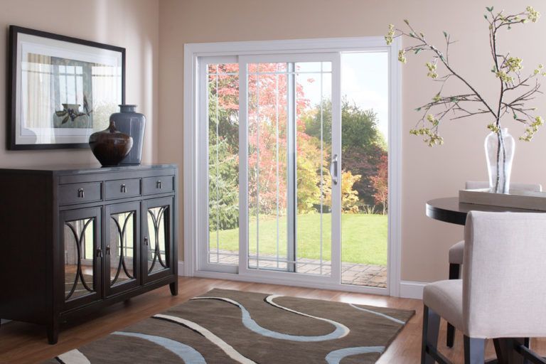 A sliding glass door opening to a yard, situated in a room with a dark sideboard, a dining chair, and a patterned rug.