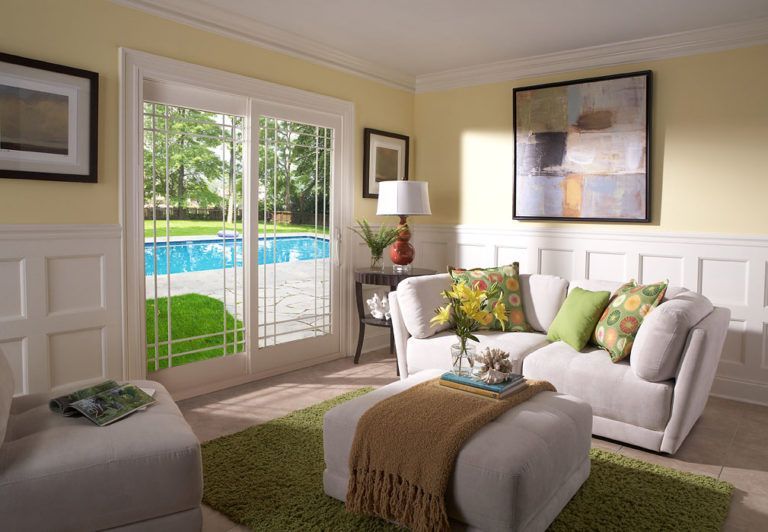 A cozy living room with a white sofa, green accents, a swimming pool view through sliding doors, and yellow walls.