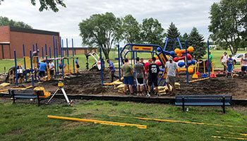 A group of people working to renovate a playground with exposed dirt, construction equipment, and colorful structures.
